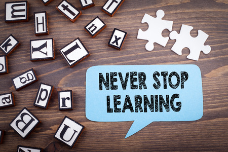 Never stop learning concept. Speech Bubble on a dark textured wooden background.