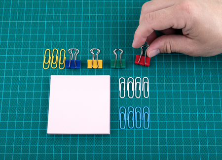 Paper clips and note sheet on checked green backgound, arrange in pedantic order by colors, mans handの写真素材