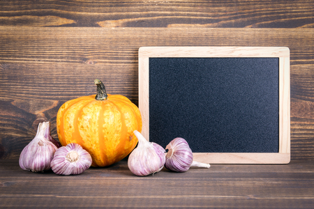 Free space for informative and marketing text on blackboard. Halloween pumpkins and garlic on a wooden backgroundの写真素材