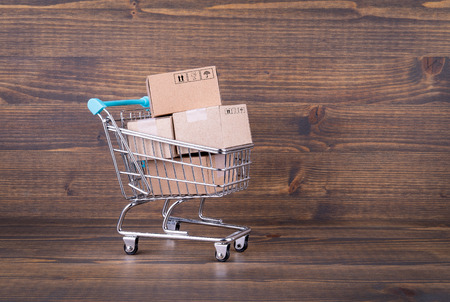 Paper boxes in a shopping cart on wooden background. Selling goods or services online over the internetの写真素材
