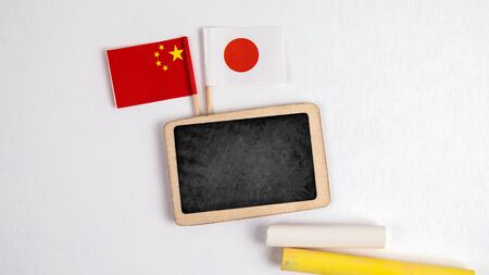 Japan and Chinese flags. Small whiteboard with chalk. Top view on a white background. Mockup, copy spaceの写真素材