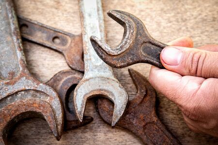 Old and rusty wrench in hand on wooden background.  Construction and hand tools, maintenance and reparing conceptの写真素材