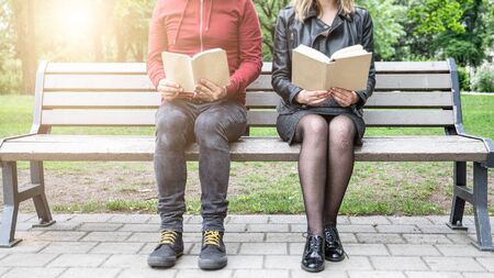Woman and man reads book sitting on a bench at the park, reading outsideの写真素材