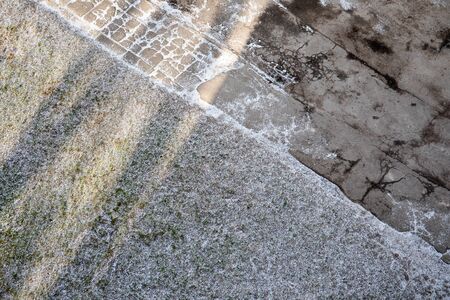 Snow-covered asphalt and green grass. City, pedestrian sidewalk, slippery and cold. Abstract season,...