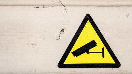 Yellow security camera sticker. Painted wooden facade. Procedures and compliance with regulationsの写真素材