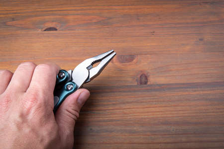 Pliers in the hand on wooden background. Hand tools for holding objects