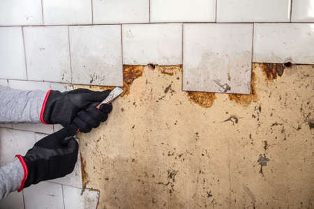 Renovation. Old dirty wall tiles. Worker with a crowbar