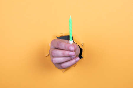 One birthday candle in a womans hand. Orange backgroundの写真素材