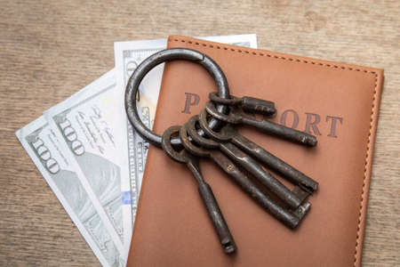 Passport, house keys and banknotes on a wooden tableの写真素材