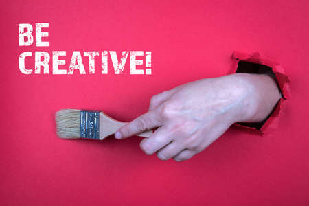 BE CREATIVE. Painters brush in a womans hand. Red backgroundの写真素材