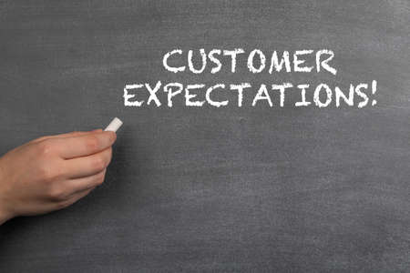 CUSTOMER EXPECTATIONS. White chalk in a womans hand. Black chalk board