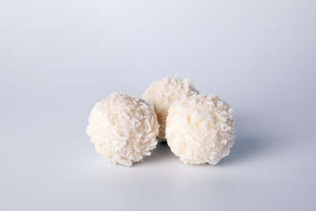 Three white candies with coconut chips, on a white background. Sweets, holidays and anniversariesの写真素材