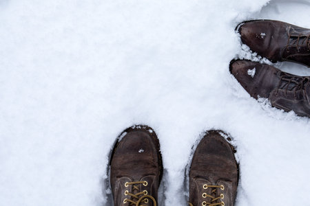 Foots in boots of two people in the snow, top view. Wintertime walk, he and sheの写真素材