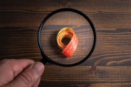 Tape measure on a wooden background. Magnifying glass in a mans hand