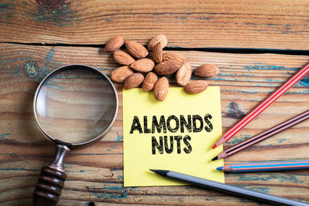 Almonds Nuts. Piece of paper, colored pencils and a magnifying glass on a wooden backgroundの写真素材