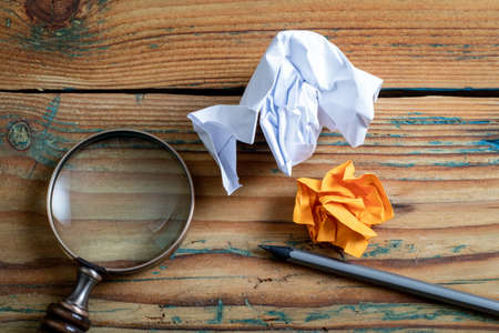 Crumpled paper, pencil and magnifying glass on a wooden background. Education, information and data search concepの写真素材