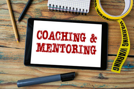 Coaching and Mentoring concept. Yellow warning tape and tablet computer on a wooden tableの写真素材