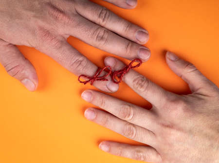 Memory and Reminder Knot. Female and male hands on an orange backgroundの写真素材