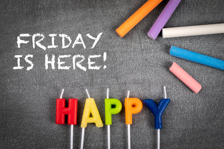 Happy, Friday is here. Colored pieces of chalk on a blackboard backgroundの写真素材