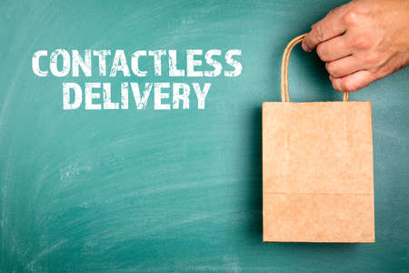 Contactless Delivery. Paper shopping bag in a mans hand. Green chalk board backgroundの写真素材