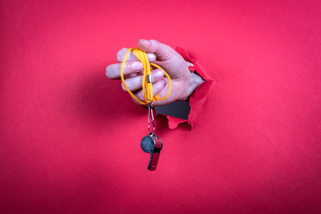 Metal whistle in a womans hand. Bright red backgroundの写真素材
