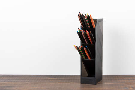 Black holder with colored pencils. Office and teaching supplies. wooden table and a white background. Copy spaceの写真素材