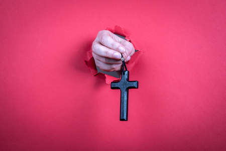 Wooden cross with a leather cord in a womans hand on a red paper backgroundの写真素材