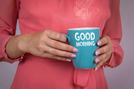 GOOD MORNING. Woman in a pink dress with a coffee mug in her handsの写真素材