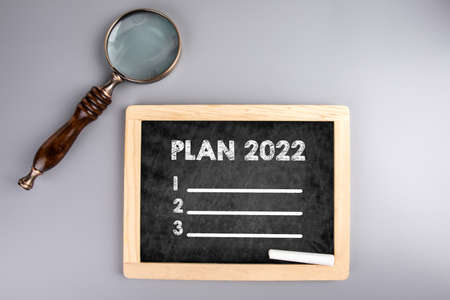 2022 plan on chalkboard, goal setting and priority in coming year. Magnifying glass on a gray table