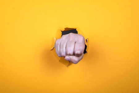 Woman s fist. Symbol of strength and greeting. torn yellow paper backgroundの写真素材