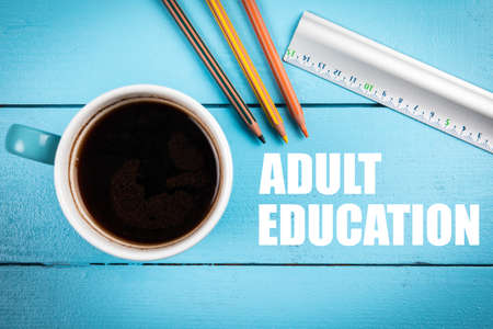 ADULT EDUCATION. Coffee mug, lined and colored pencils on a wooden table