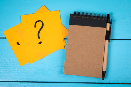 Notepad and note papers with question marks. Blue board tableの写真素材