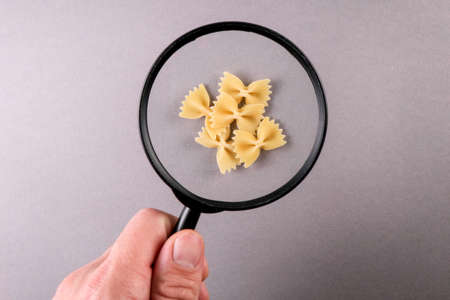 Farfalle Pasta on a gray background. Magnifying glass in a mans handの写真素材