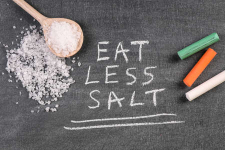 Eat Less Salt. Wooden spoon and chalk pieces on a chalk boardの写真素材
