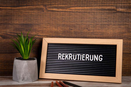 RECRUITMENT. Text in German. Green plant and pencils on a wooden backgroundの写真素材