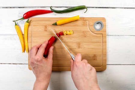 Womans hands with a knife cut pepper on a bamboo cutting board. Spices and organic productの写真素材