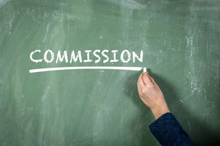 Commission. Business woman writes text with chalk on a green chalkboard