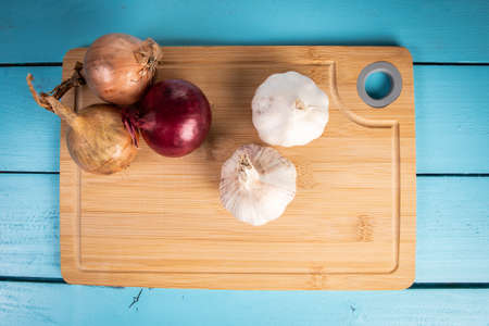 Onions and garlic on a bamboo cutting board, blue wooden backgroundの写真素材