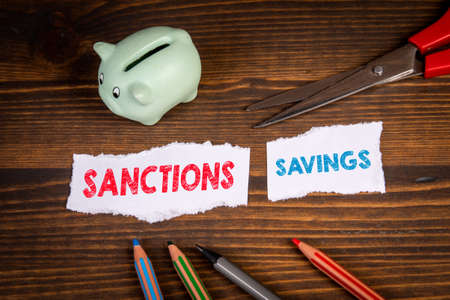 Economic sanctions and savings concept. Cut sheet of paper, scissors and piggy bank on a wooden backgroundの写真素材