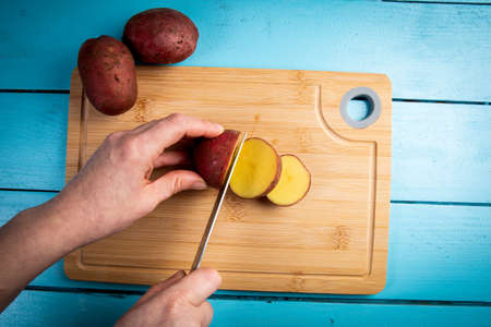 women s hands cut the potatoes into slices. bamboo cutting boardの写真素材