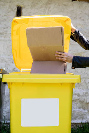 Waste sorting. Woman puts cardboard box in a yellow container