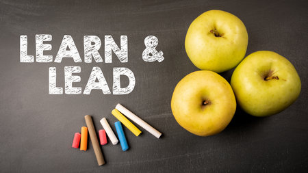 Learn and Lead. Three apples and colored pieces of chalk on a dark blackboard