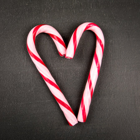 Two candy canes in the shape of a heart on a dark chalkboard backgroundの写真素材