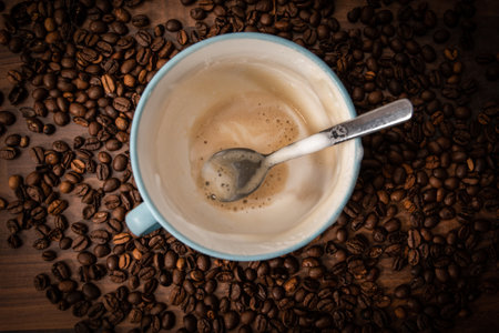 Milk foam and a spoon in a coffee cup. Coffee beans backgroundの写真素材