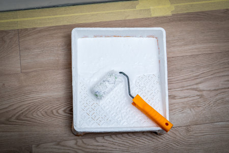 Paint roller in paint tray with white color on wooden floorの写真素材