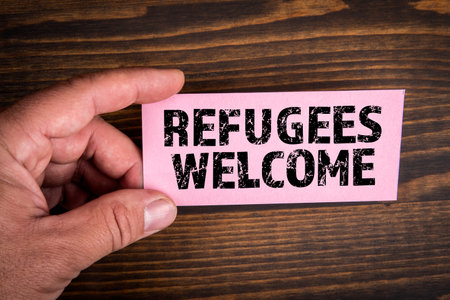 Refugees Welcome. Text on pink paper. Wood texture backgroundの写真素材