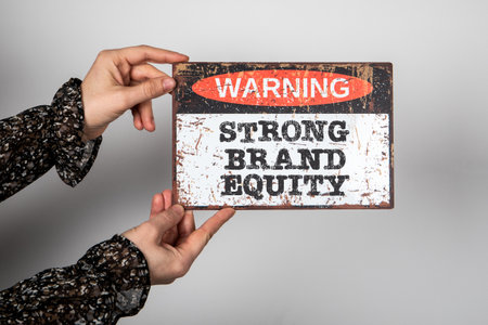 STRONG BRAND EQUITY. Warning sign with text on a white background in a womans handの写真素材
