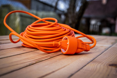 Orange electric cable, extension cord rolled up on a wooden table
