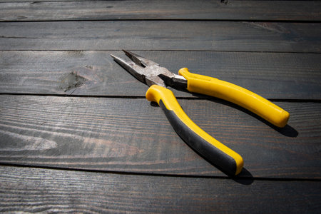 Pliers with yellow handles on a dark wooden texture background