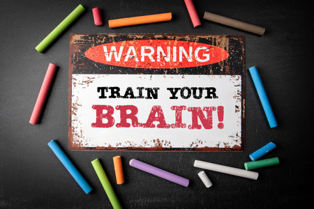 Train Your Brain. Metal warning sign and colored pieces of chalk on a dark chalkboard backgroundの写真素材